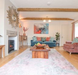 A living room with a blue sofa pink armchairs a wooden coffee table and wall art at Riviere Barton in Hayle