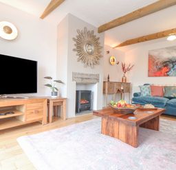 A living room with a blue sofa a wooden coffee table with fruit and chess set a wooden TV stand with a TV and a fireplace at Riviere Barton in Hayle