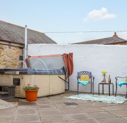 An outdoor patio with a hot tub a potted plant two chairs with cushions and towels and a small table with flowers and drinks at Riviere Barton in Hayle