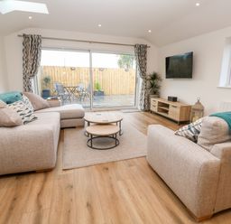 A living room with two beige sofas a wooden coffee table and a mounted TV at Puffins Rest in Goldsithney