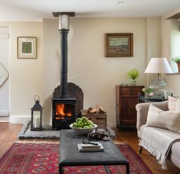 A living room with a wood stove fire a bowl of green apples on a coffee table and a sofa with cushions at Hawthorn Cottage at Collihole in Chagford