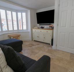 A living room with a sofa a bay window with white shutters a white cabinet with decorations and a wall mounted TV at Belvedere Cottage in Weymouth