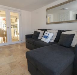 A living room with a dark sofa with cushions and glass doors leading to a kitchen at Belvedere Cottage in Weymouth