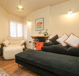 A living room with a black sofa and white armchair near an orange stove at Josie in Pentewan