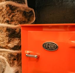 A close up of an orange Everhot stove next to a stone wall at Josie in Pentewan