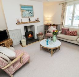 A living room with a fireplace a sofa armchairs a round coffee table and a television at Eider Cottage in Warkworth