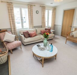 A sitting room with a sofa armchairs a round coffee table and windows with curtains at Eider Cottage in Warkworth