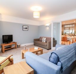 A living room with sofas a wooden coffee table a television on a stand and an armchair with cushions at 11 The Craighurst in Southwold
