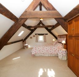A bedroom with exposed wooden beams a bed with floral bedding wooden wardrobe and chairs at Anvil Cottage in Gatcombe near Blakeney