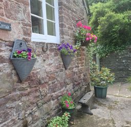 A garden with hanging planters and a stone wall at Anvil Cottage in Gatcombe near Blakeney