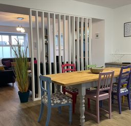 A dining area with a wooden table and colorful chairs next to a living space with sofas at 2A Front Street in Embleton