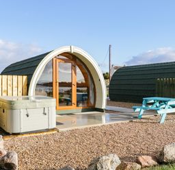 A curved wooden pod with glass doors a hot tub and a blue picnic table outside at The Wheelhouse Pod No 1 in Burtonport County Donegal