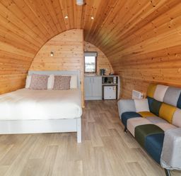 A wooden pod interior with a bed, a kitchenette, and a multicolored sofa at The Wheelhouse Pod No 1 in Burtonport County Donegal