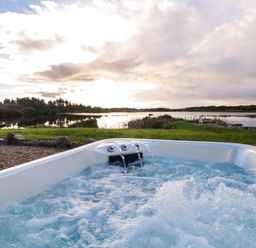 An outdoor hot tub with water jets near a grassy area and a body of water at The Wheelhouse Pod No 2 in Burtonport County Donegal