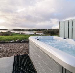 An outdoor hot tub near a gravel path with a lake and grassy area in the background at The Wheelhouse Pod No 3 in Burtonport County Donegal