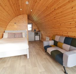 A wooden pod interior with a bed a colorful patchwork sofa and a small kitchenette at The Wheelhouse Pod No 3 Burtonport County Donegal