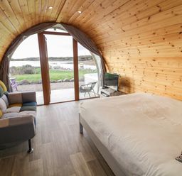 A bedroom with a bed sofa and television overlooking a lake at The Wheelhouse Pod No 3 in Burtonport County Donegal