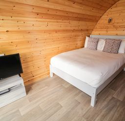 A bedroom with a bed and two pillows and a TV on a stand against a wooden wall at The Wheelhouse Pod No 3 Burtonport County Donegal