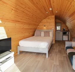A wooden pod interior with a bed, a television, a sofa, and a kitchenette at The Wheelhouse Pod No 4 in Burtonport County Donegal