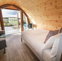 A wooden interior room with a bed and a sofa near an open door looking outside at The Wheelhouse Pod No 4 in Burtonport County Donegal
