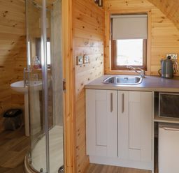 A small kitchen area with a sink microwave fridge and kettle next to a bathroom with shower and sink at The Wheelhouse Pod No 4 in Burtonport County Donegal