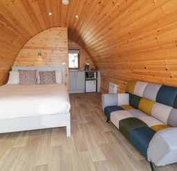 A wooden pod interior with a bed and pillows a small kitchenette and a multicolored sofa at The Wheelhouse Pod No 7 in Burtonport County Donegal