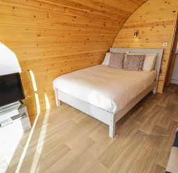 A bedroom with a bed two pillows a TV on a stand and a doorway to a kitchen at The Wheelhouse Pod No 7 Burtonport County Donegal