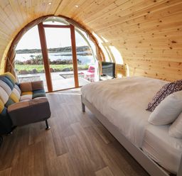 A pod interior with a bed sofa and television facing glass doors showing outdoor water view at The Wheelhouse Pod No 7 Burtonport County Donegal