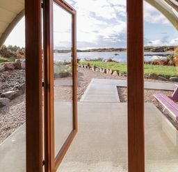 A view through glass doors opening to a patio with a purple picnic table and a pathway leading to a lake at The Wheelhouse Pod No 9 Burtonport County Donegal