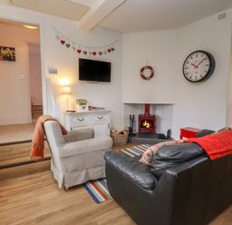 A living room with a leather sofa a checkered armchair a fireplace and a wall clock at The Little White Cottage in Milton-Under-Wychwood