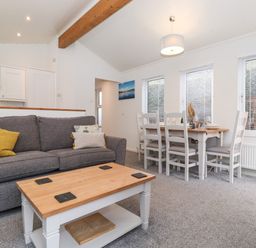 A living room with a gray sofa and a wooden coffee table next to a dining table with white chairs at Bowness Bay Lodge Oakside 16 Fallbarrow Park near Bowness-On-Windermere