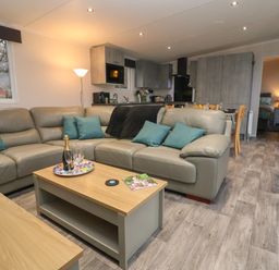 A living room with a gray sectional sofa blue pillows a wooden coffee table and an open kitchen at Holmside Audley Brow near Market Drayton