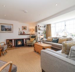 A living room with sofas chairs a coffee table a fireplace and a large window at Beta Cottage in Walberswick