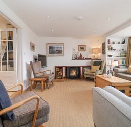 A living room with armchairs a sofa a wooden coffee table a fireplace and shelves at Beta Cottage in Walberswick