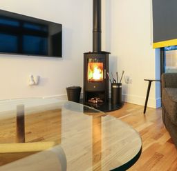 A living room with a wall-mounted TV wood burning stove gray sofa and glass coffee table at 2 Strathtay Lodges in Aberfeldy