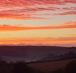 A landscape of fields and hills under a sky with orange and pink clouds at sunset at South Holm Moreleigh