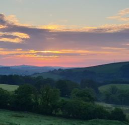 A countryside landscape with rolling hills and trees under a sunset sky at South Holm in Moreleigh