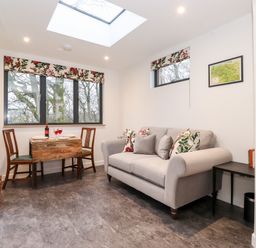 A sitting area with a sofa and small dining table with two chairs near windows at Herdwick Cabin in Hutton John near Penruddock