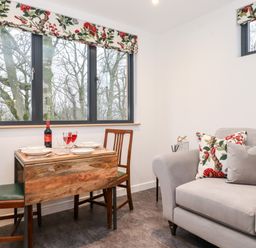 A small dining table with two chairs near windows and a gray sofa with floral cushions at Herdwick Cabin in Hutton John near Penruddock