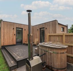 A wooden deck with two chairs and a hot tub outside a wooden cabin at Herdwick Cabin in Hutton John near Penruddock