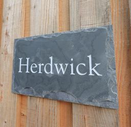A black stone plaque with the word Herdwick mounted on a wooden wall at Herdwick Cabin in Hutton John near Penruddock
