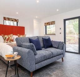 A bedroom with a red headboard bed a blue sofa and glass doors showing a garden at The Gardener's Retreat in Hutton John near Penruddock