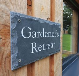 A wooden wall with a slate sign reading Gardeners Retreat beside a window at The Gardeners Retreat in Hutton John near Penruddock
