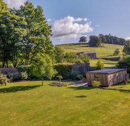 A garden with grass trees a wooden shed and a stone wall with hills in the background at The Gardener's Retreat in Hutton John near Penruddock