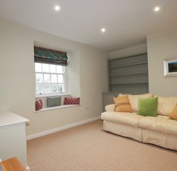 A living room with a cream sofa with cushions a window seat with cushions a television on a white unit and a built in shelving unit at Tretoil Farm House in Bodmin