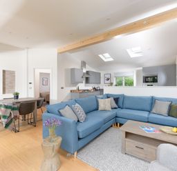 An open plan living room and kitchen with a blue sectional sofa wooden coffee table dining table and gray kitchen cabinets at 5 Southern Place in Dobwalls