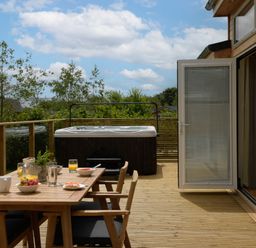 An outdoor deck with a wooden dining table set food and drinks and a hot tub at 5 Southern Place in Dobwalls