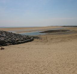 A sandy beach with a rocky embankment and tidal pools by the sea at Swn Y Mor in Burry Port