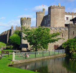A stone castle with turrets a flag on top surrounded by a grassy area with trees picnic tables and a pond with a fence at Watermouth Castle Bassett Apartment in Berrynarbor near Ilfracombe