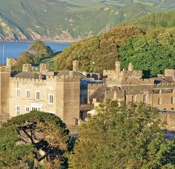 An exterior view of a castle surrounded by trees and ocean at Watermouth Castle, Bassett Apartment, Berrynarbor near Ilfracombe